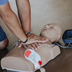 Hands demonstrating CPR technique on training mannequin with AED device