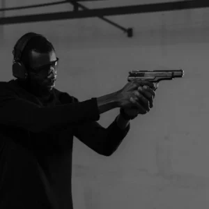 Adult man wearing protective gear practices shooting indoors with a handgun